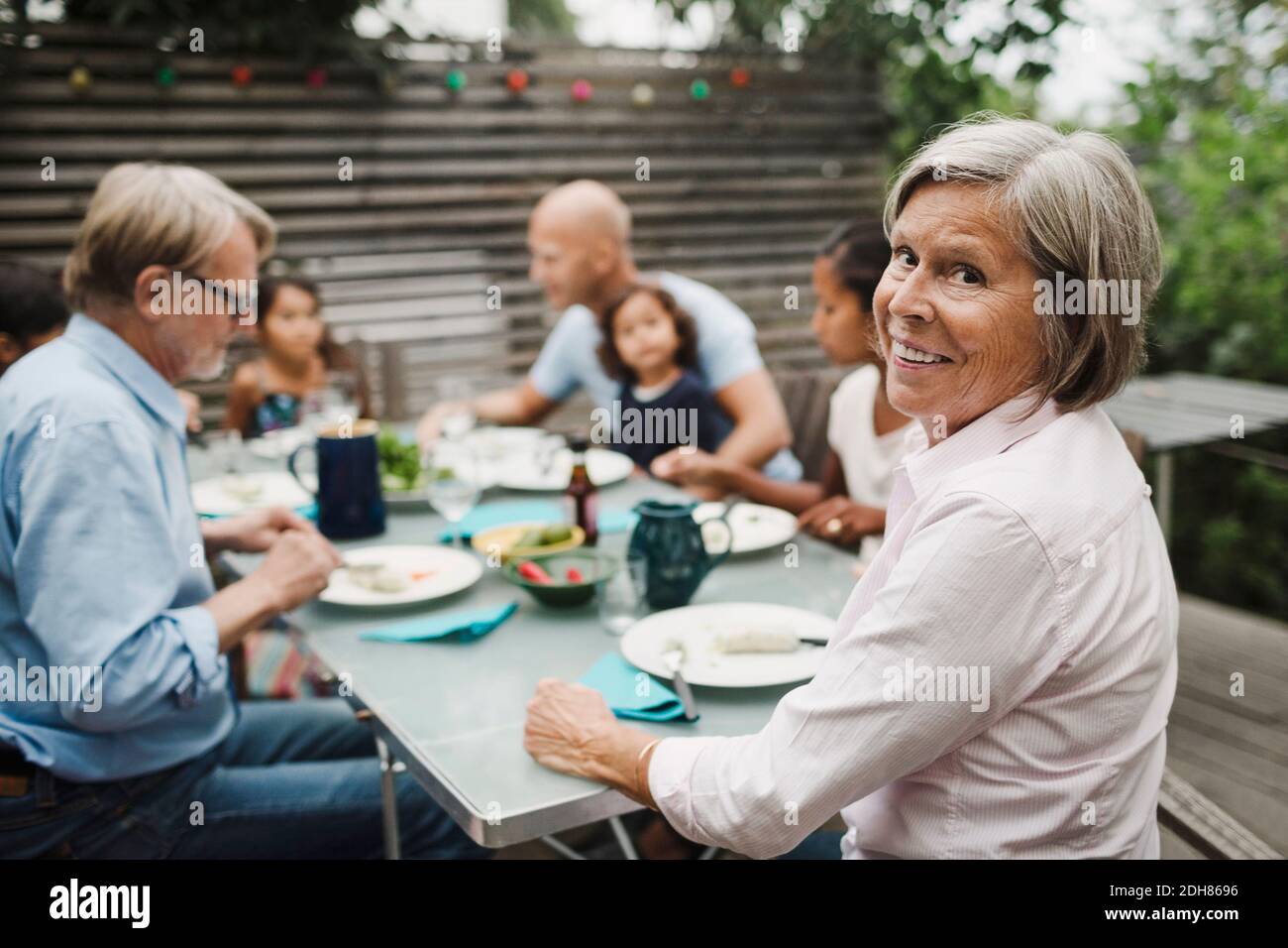 Ritratto di felice anziana seduta con la famiglia all'aperto tavolo da pranzo Foto Stock