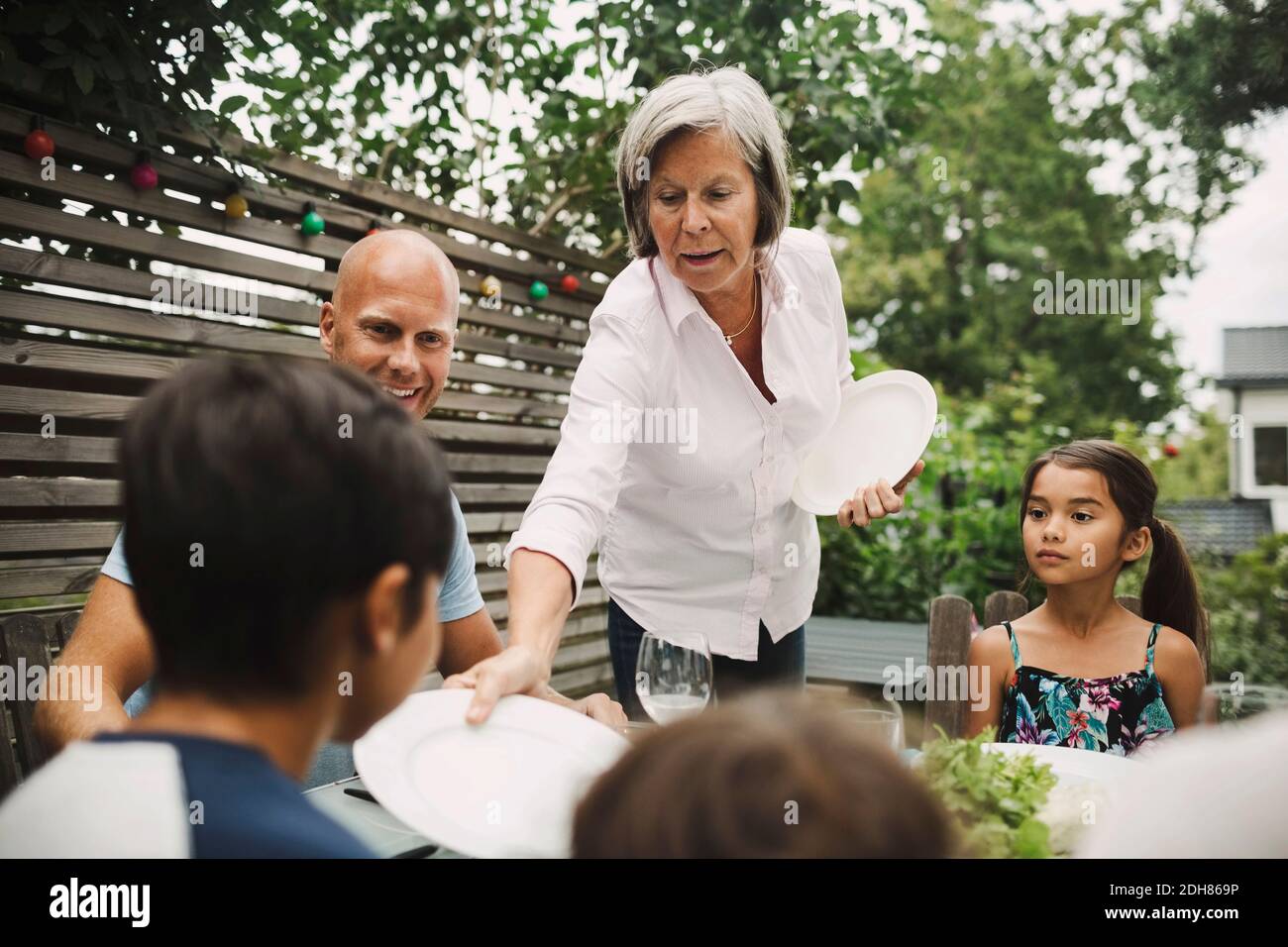 Donna anziana che dà piatto al nipote al tavolo da pranzo all'aperto Foto Stock