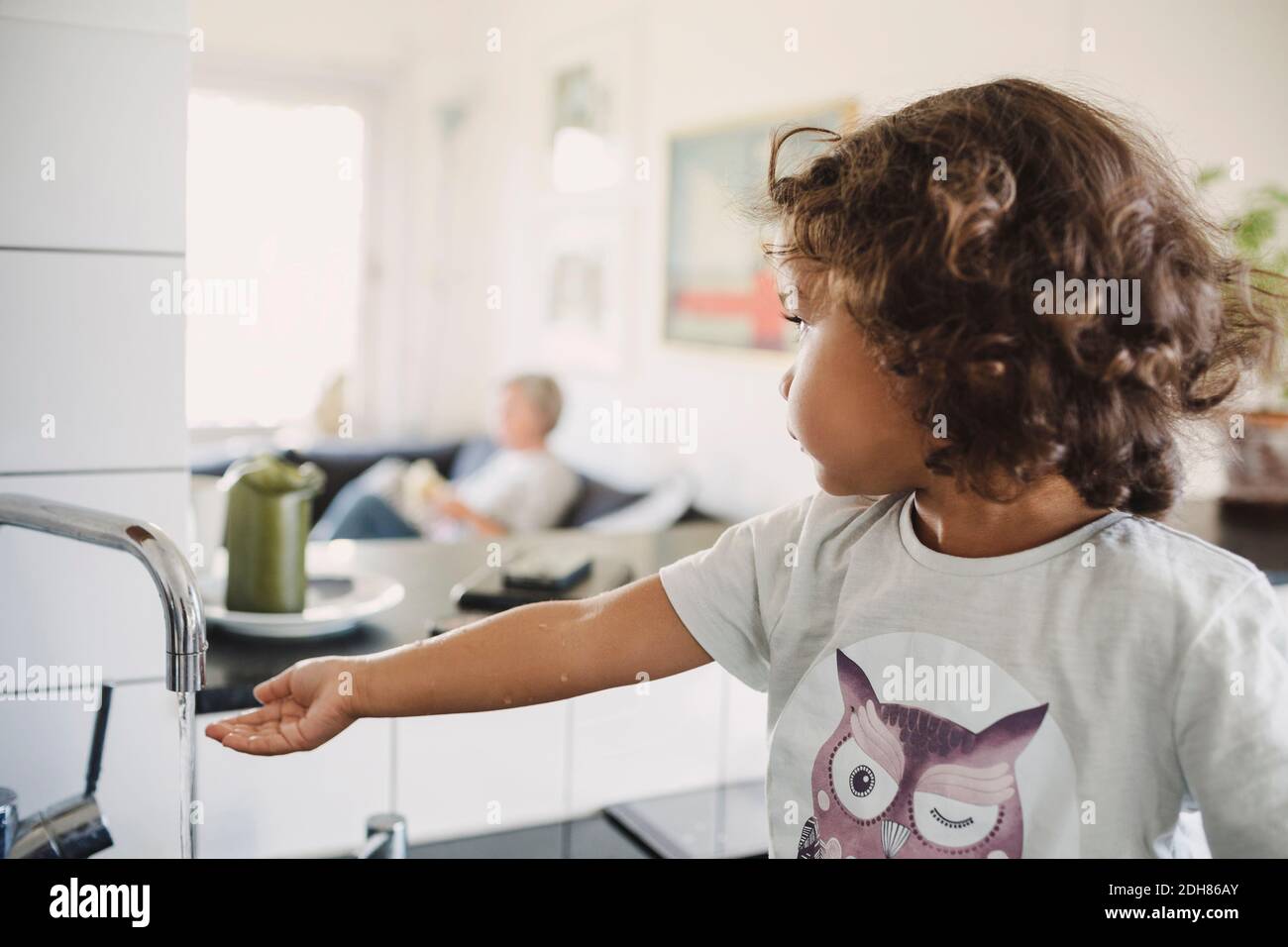 Ragazza che guarda via mentre lavano la mano sotto il rubinetto a casa Foto Stock