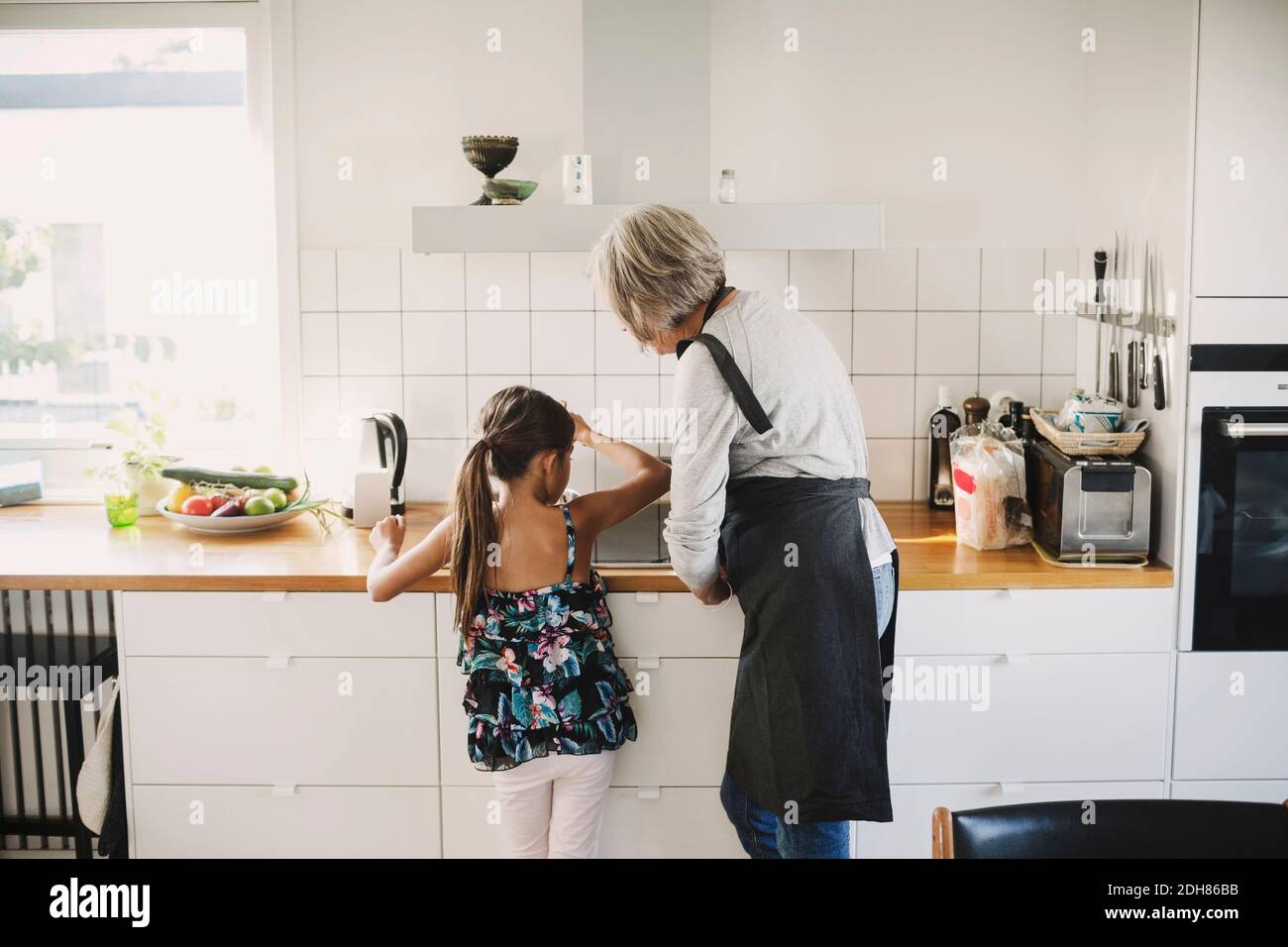 Vista posteriore della ragazza in piedi con nonna che prepara il cibo in cucina Foto Stock
