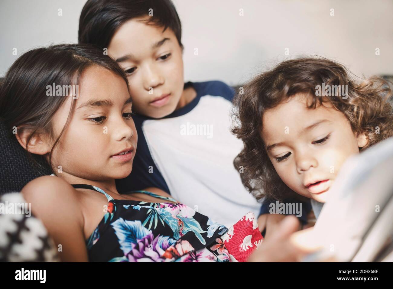 Fratelli e sorelle che usano il tablet digitale sul divano di casa Foto Stock