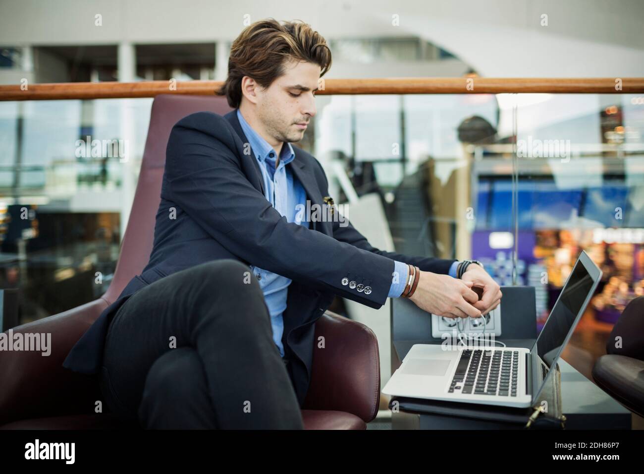 Uomo d'affari che collega la spina al computer portatile nella lobby dell'aeroporto Foto Stock
