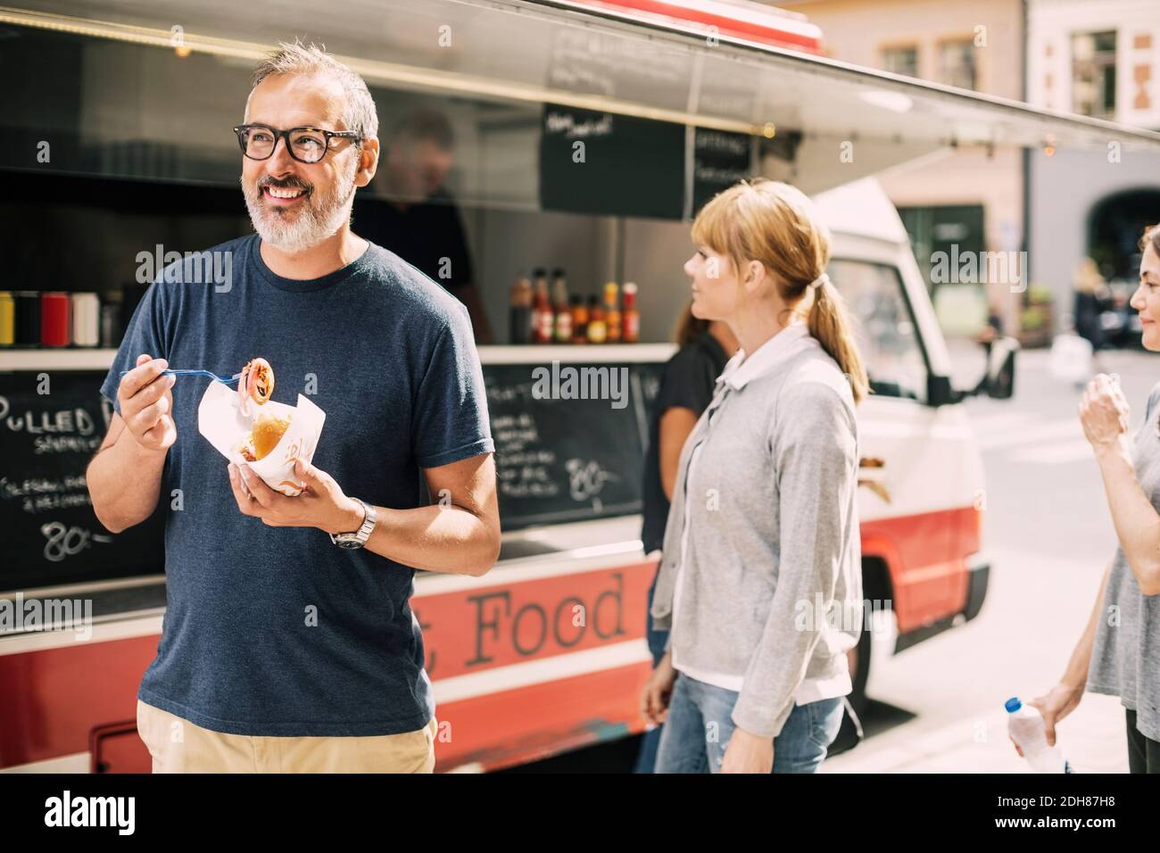 Uomo maturo che mangia cibo in piedi contro camion in strada Foto Stock