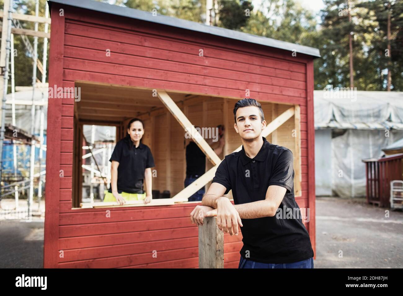 Ritratto di sicuro studente di carpenteria appoggiato su tavola con compagno di classe in background Foto Stock