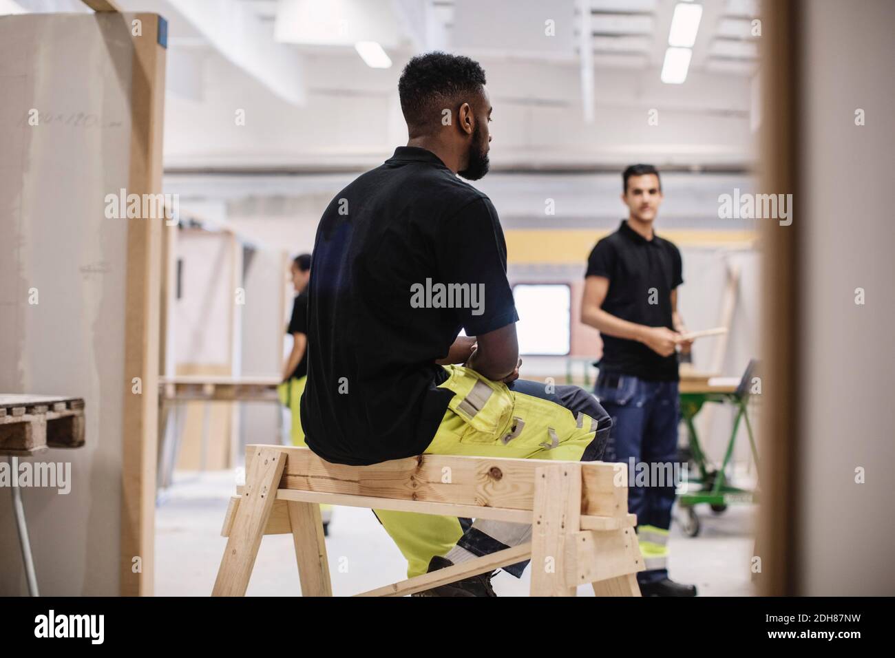 Vista posteriore di studente di carpenteria seduto su struttura in legno a. officina Foto Stock