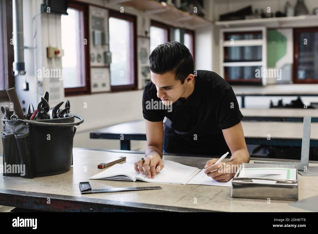 Giovane studente di scuola superiore che scrive nel libro al workshop Foto Stock