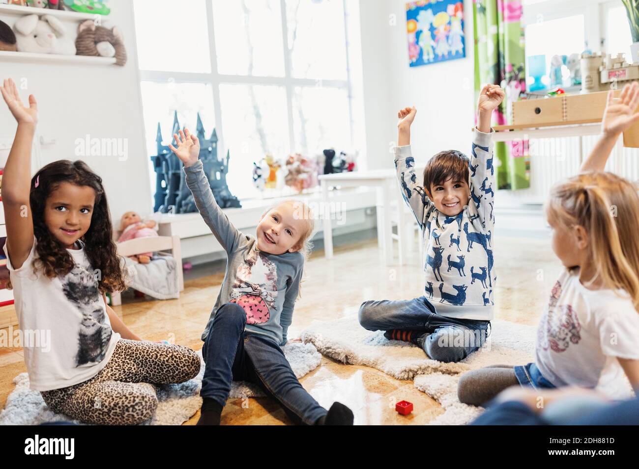 Felici i bambini che alzano le mani mentre si siedono in preschool Foto Stock