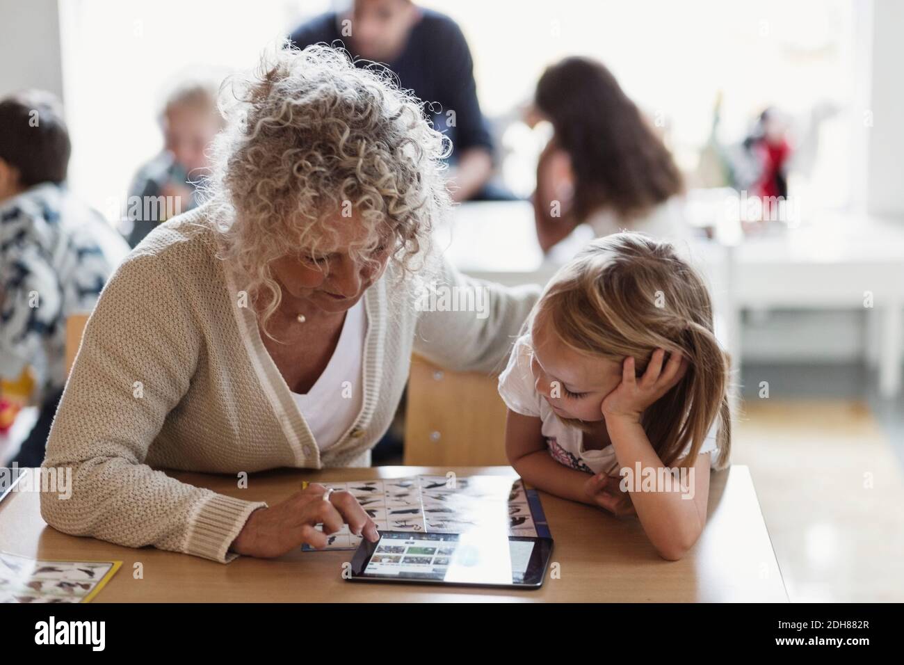 Insegnante senior che utilizza un tablet digitale con uno studente in età prescolare Foto Stock