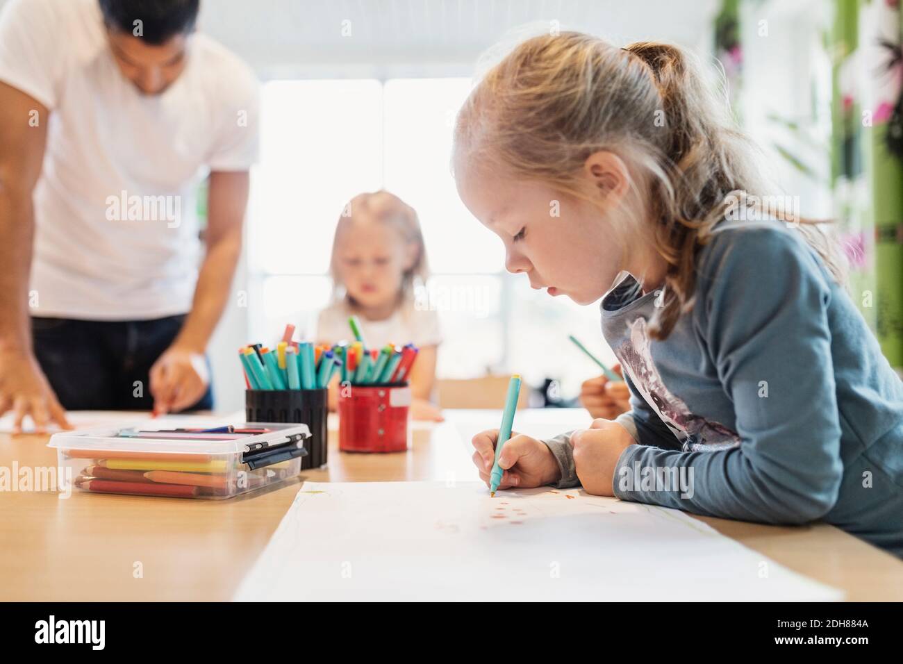 Ragazza con pennarello in classe di disegno con compagno di classe e insegnante in background Foto Stock