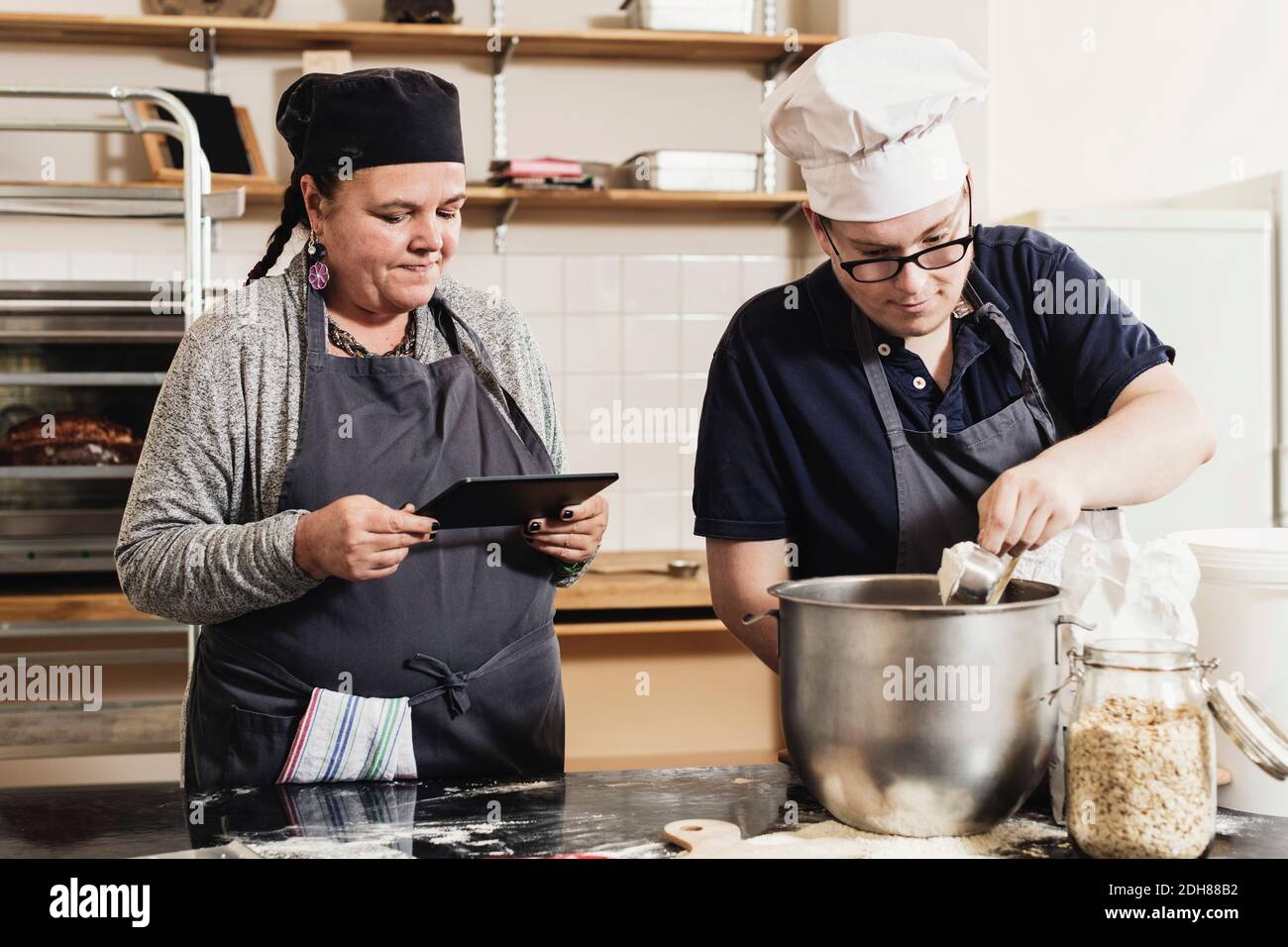 Donna che tiene un tablet digitale mentre coworker cucina cibo in cucina Foto Stock