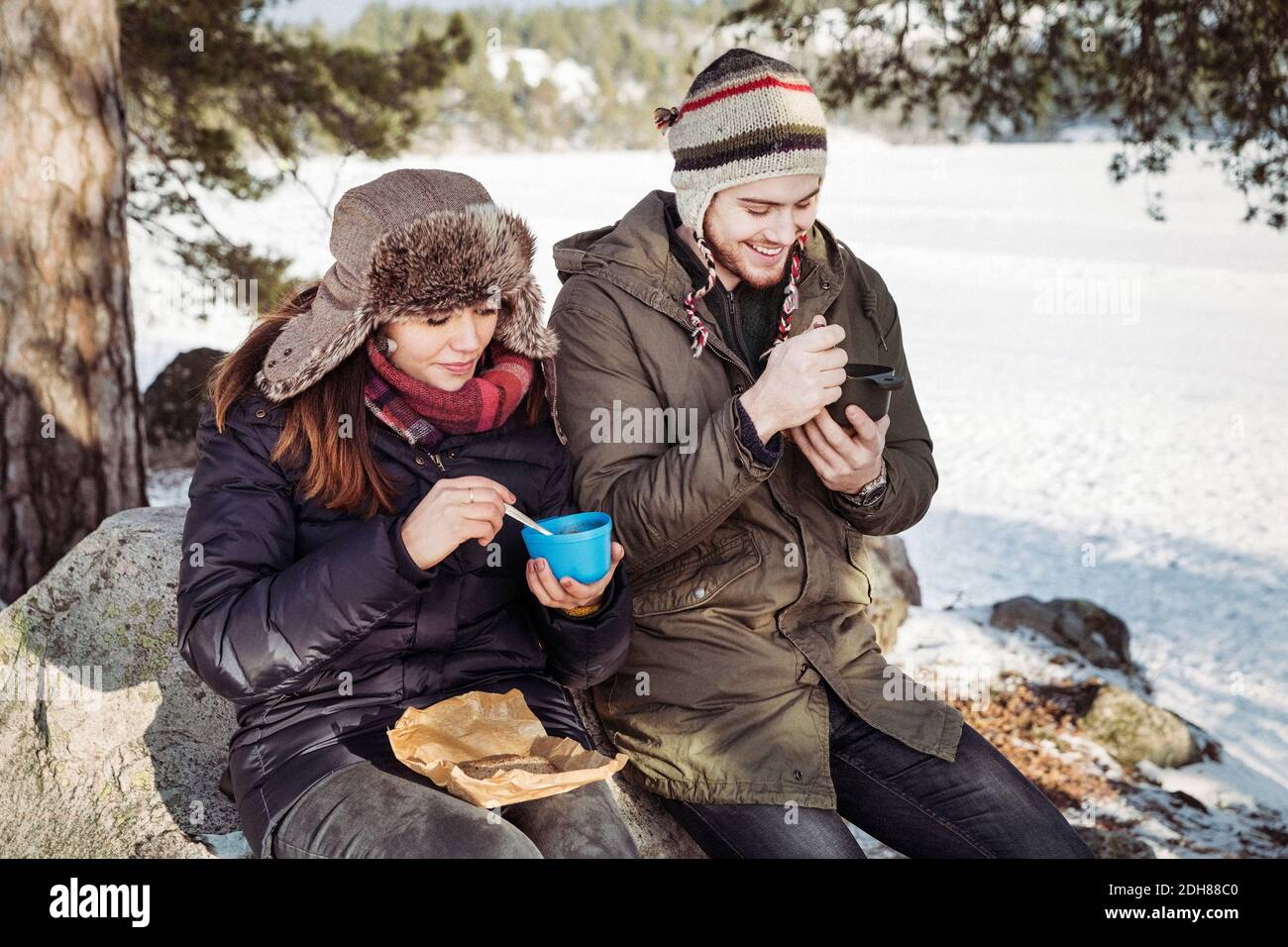 Coppia avendo cibo mentre si siede sulla roccia a campo durante inverno Foto Stock