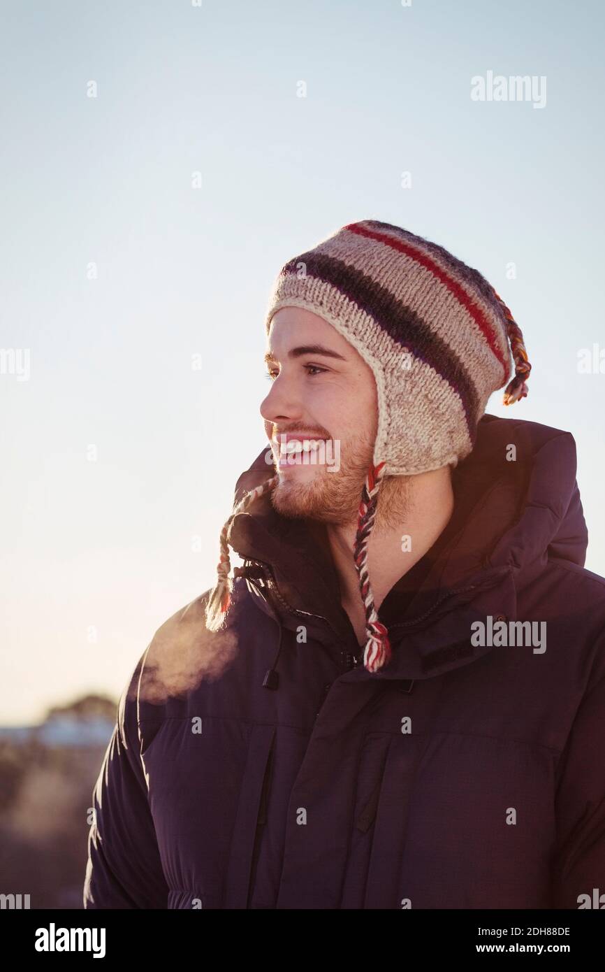 Felice giovane uomo che guarda via contro il cielo chiaro durante l'inverno Foto Stock