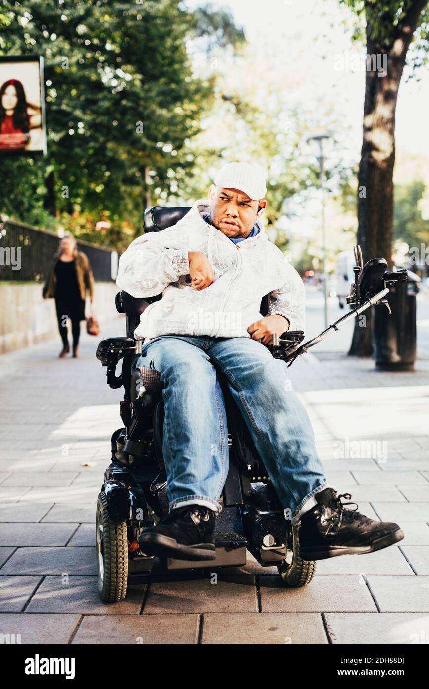 Vista frontale di un uomo disabili su sedia a rotelle sul marciapiede città Foto Stock