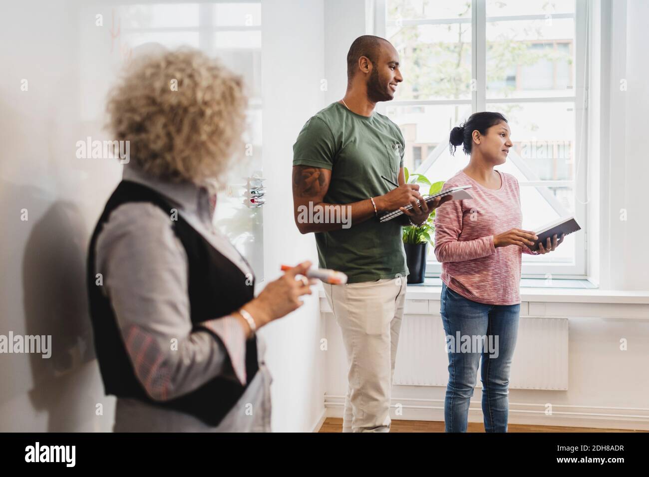 Insegnante che guarda gli studenti che leggono contro la lavagna in classe di lingua Foto Stock