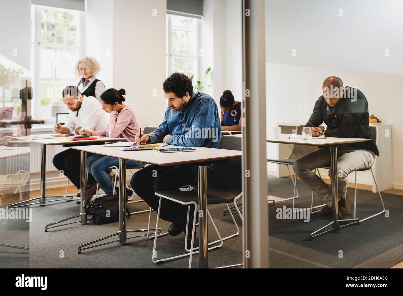 Insegnante che guarda gli studenti che scrivono in classe di lingua Foto Stock