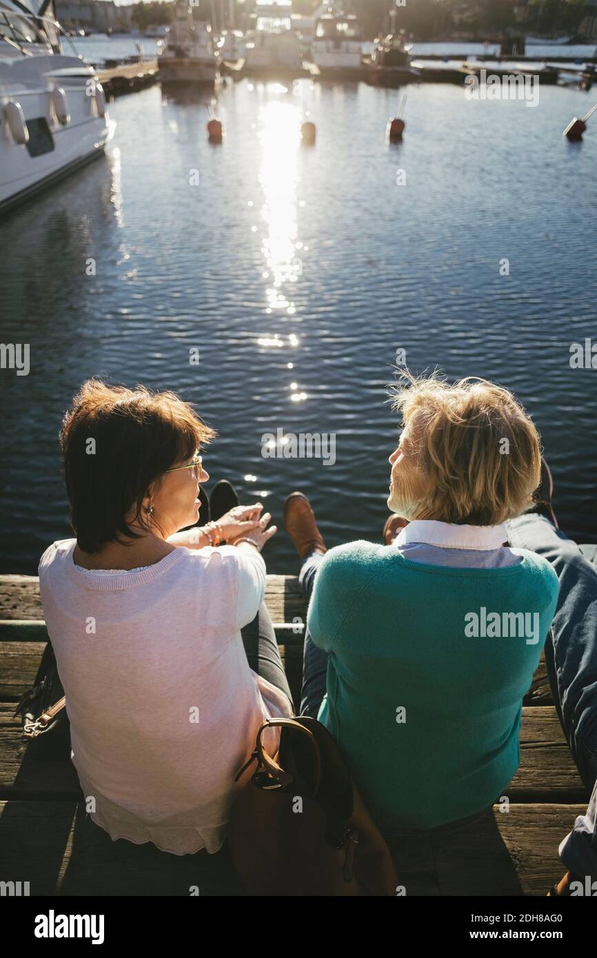 Vista posteriore delle donne anziane che parlano mentre si siedono sul molo Foto Stock