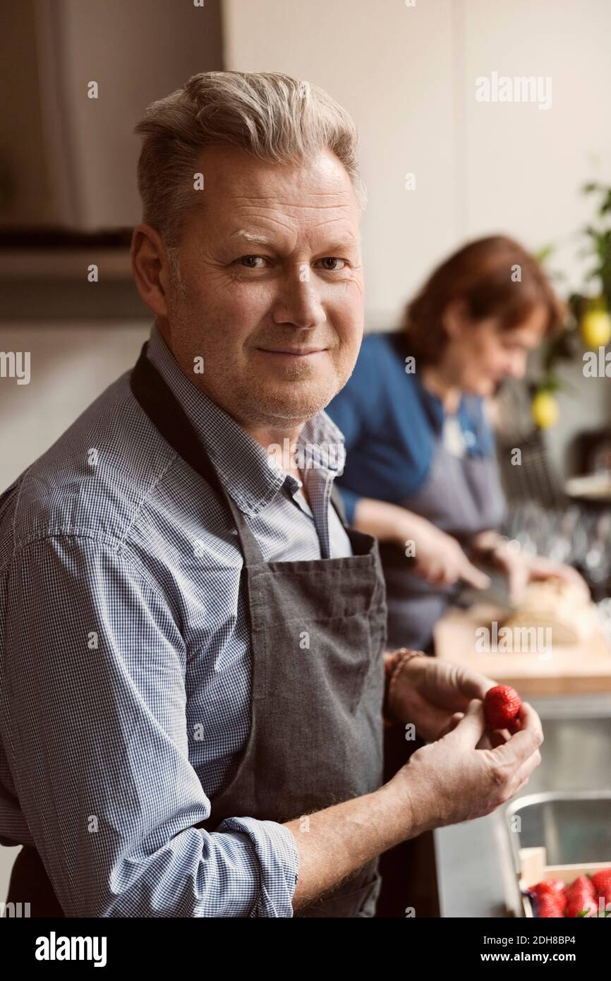 Ritratto di uomo maturo che tiene la fragola con la donna sullo sfondo Foto Stock