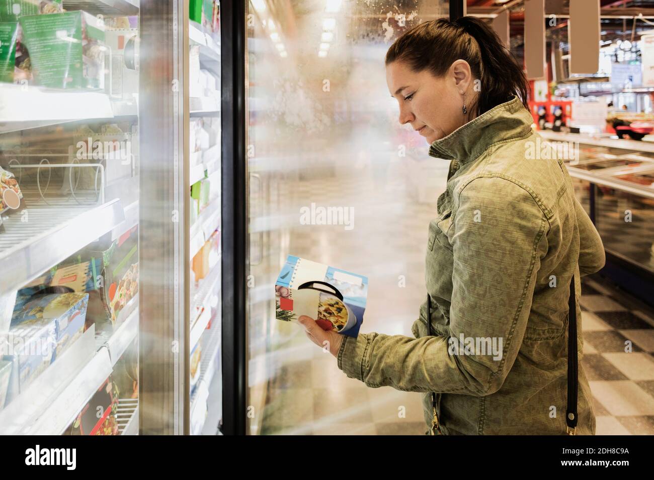 Vista laterale della donna che legge l'etichetta del cibo nella sezione refrigerata Foto Stock