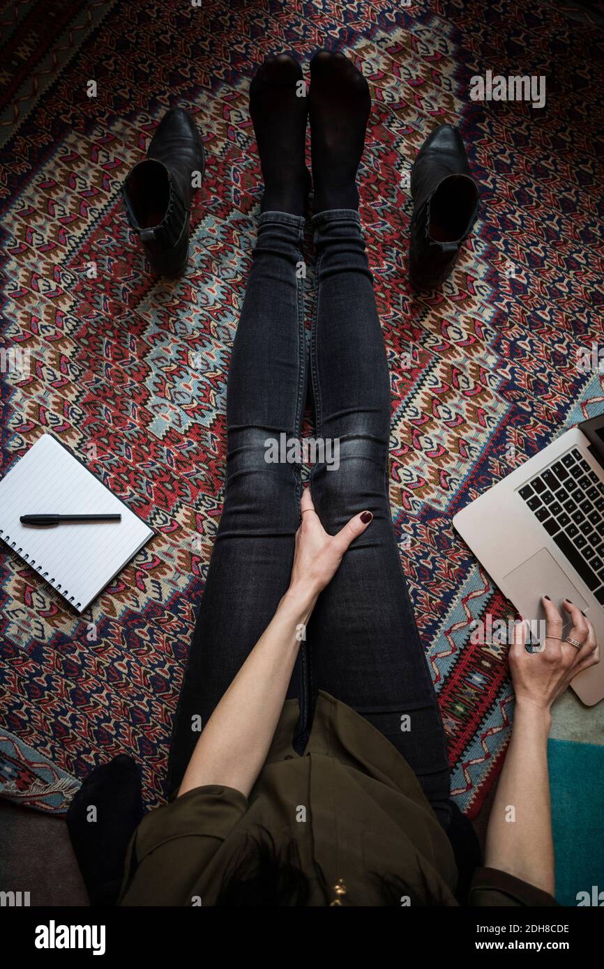 Sezione bassa del blogger che usa il laptop mentre si siede sul tappeto Foto Stock
