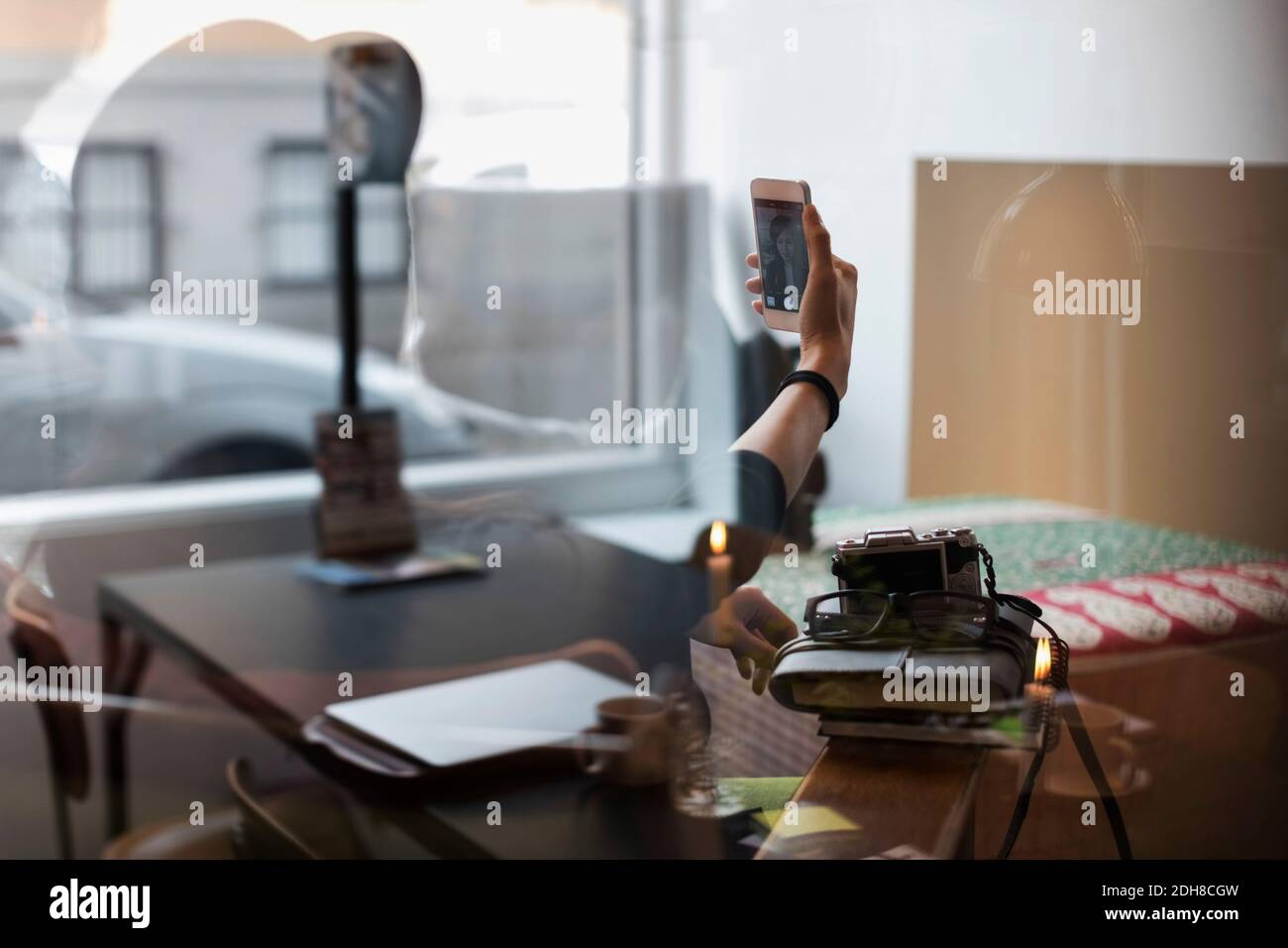 Donna che prende selfie in ufficio creativo visto attraverso il vetro Foto Stock