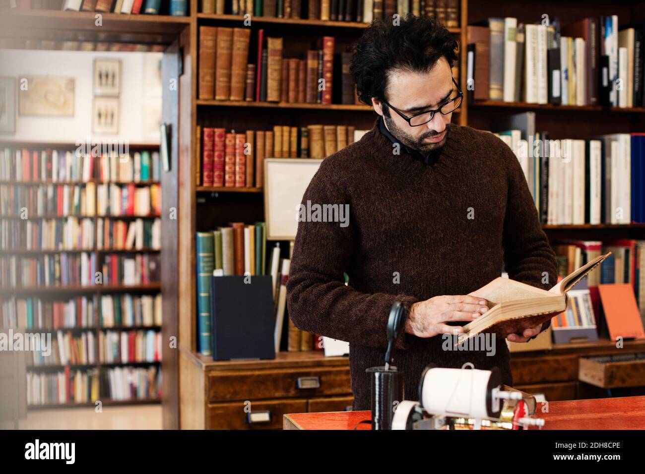 Il proprietario legge il libro mentre è in piedi in negozio Foto Stock