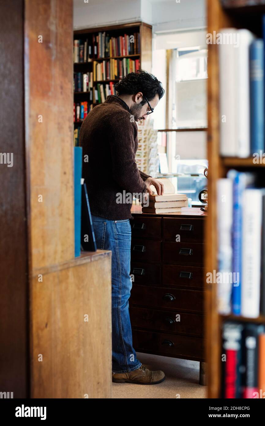 Uomo che legge libro mentre in piedi visto dagli scaffali Foto Stock