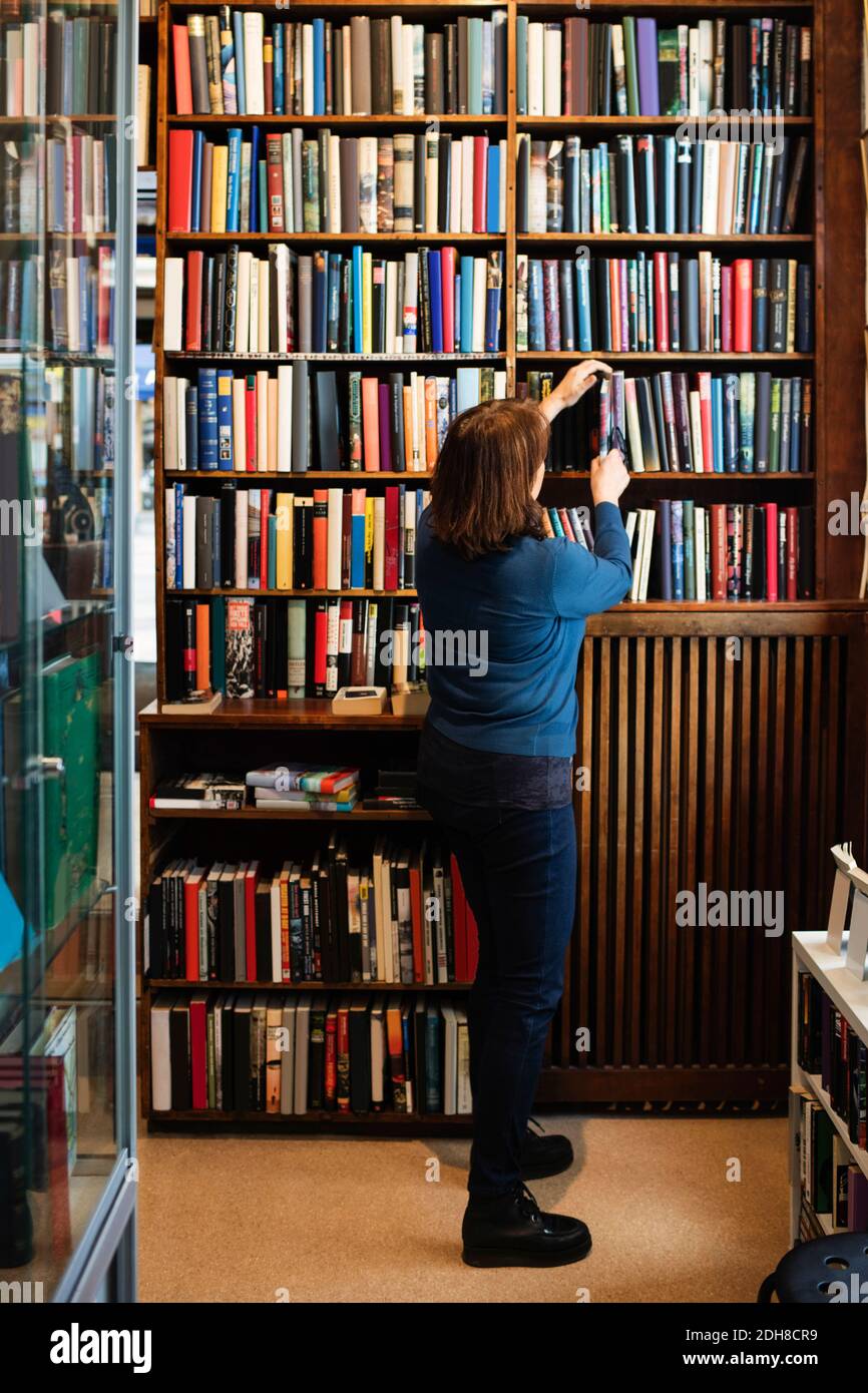 Vista posteriore della libreria che dispone i libri sullo scaffale in negozio Foto Stock