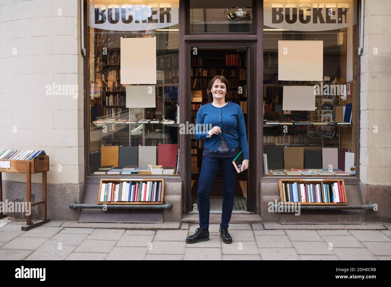 Ritratto di donna felice che tiene il libro mentre si trova fuori libreria Foto Stock