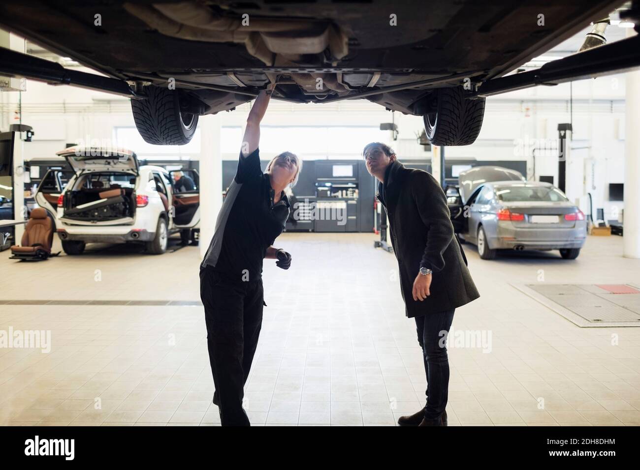 Donna esperta e cliente in piedi sotto l'auto presso il negozio di riparazione Foto Stock