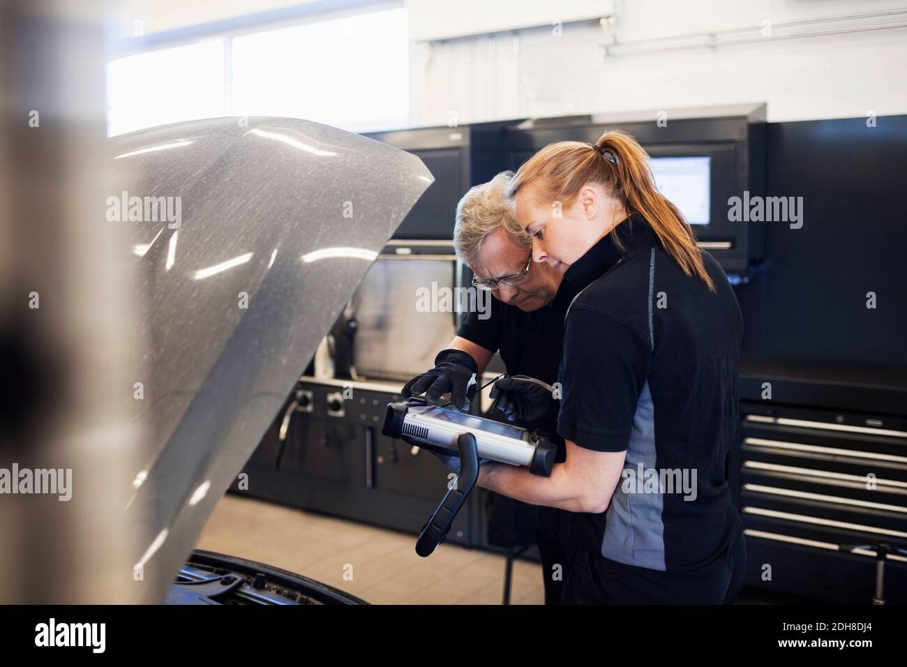 I meccanici utilizzano la tecnologia mentre esaminano l'automobile in negozio Foto Stock