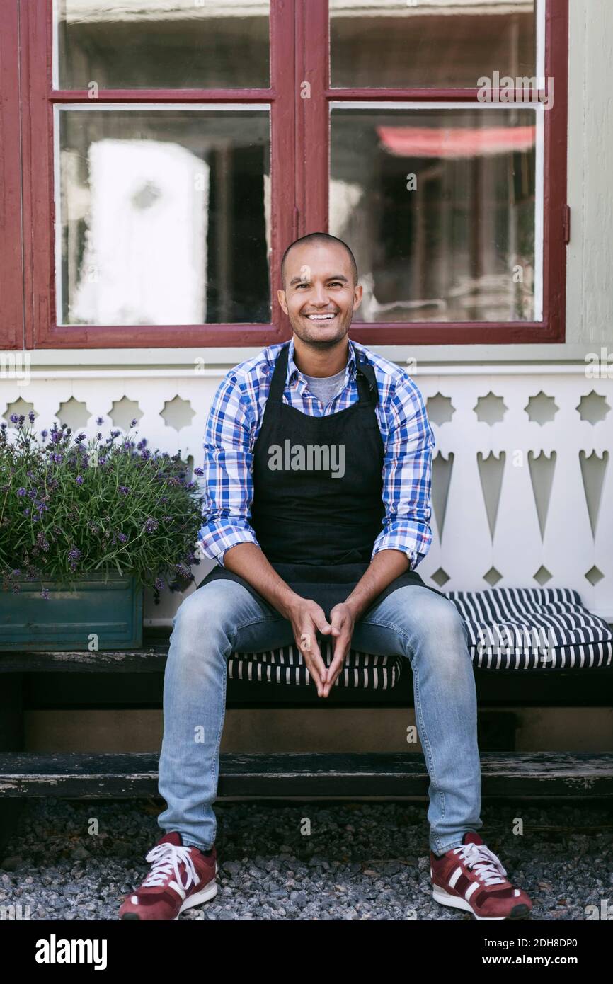 Ritratto di uomo sorridente seduto su una panchina contro la finestra esterna caffè Foto Stock