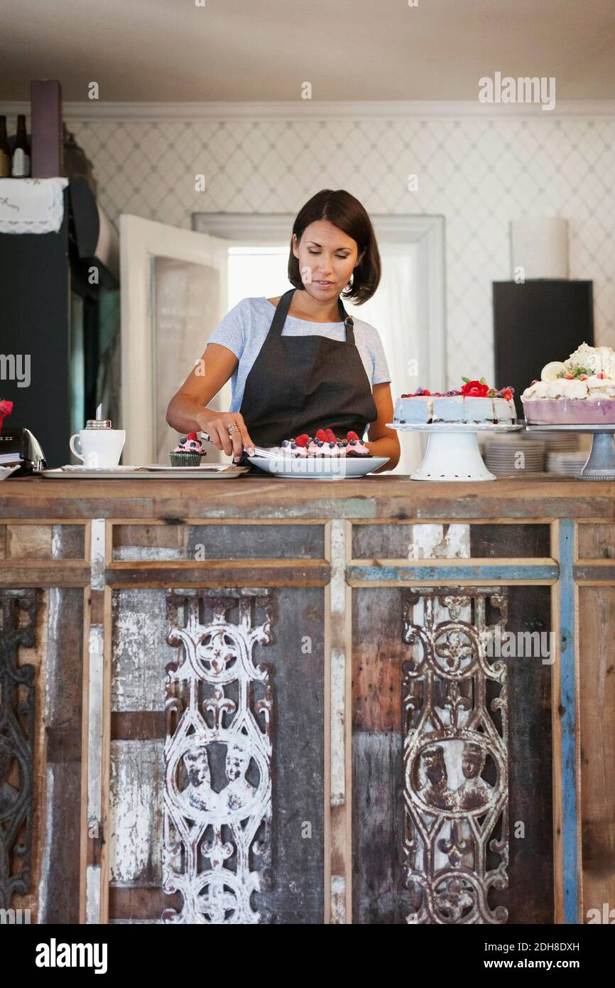 Panettiere femminile concentrato che serve muffin mentre si trova dietro il bancone caffè Foto Stock