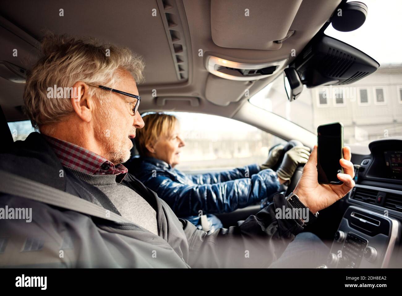 Uomo che tiene lo smartphone mentre si siede da una donna anziana che guida auto in città Foto Stock
