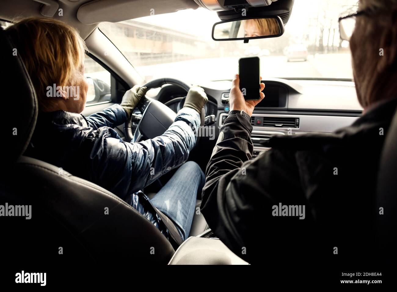 Donna anziana che guida l'auto mentre si siede da un uomo che prende selfie tramite smartphone Foto Stock