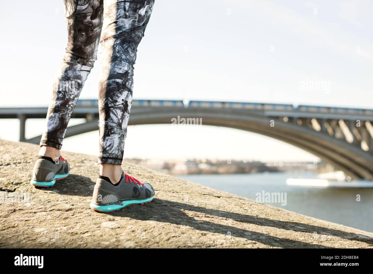 Sezione bassa di donna che indossa scarpe sportive in piedi su roccia in collina contro il ponte Foto Stock