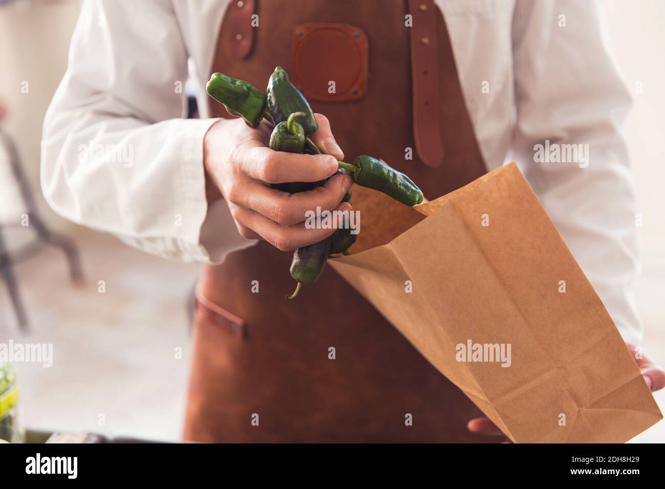 Sezione centrale del venditore che mette i peperoncini verdi in sacchetto di carta al negozio di alimentari Foto Stock