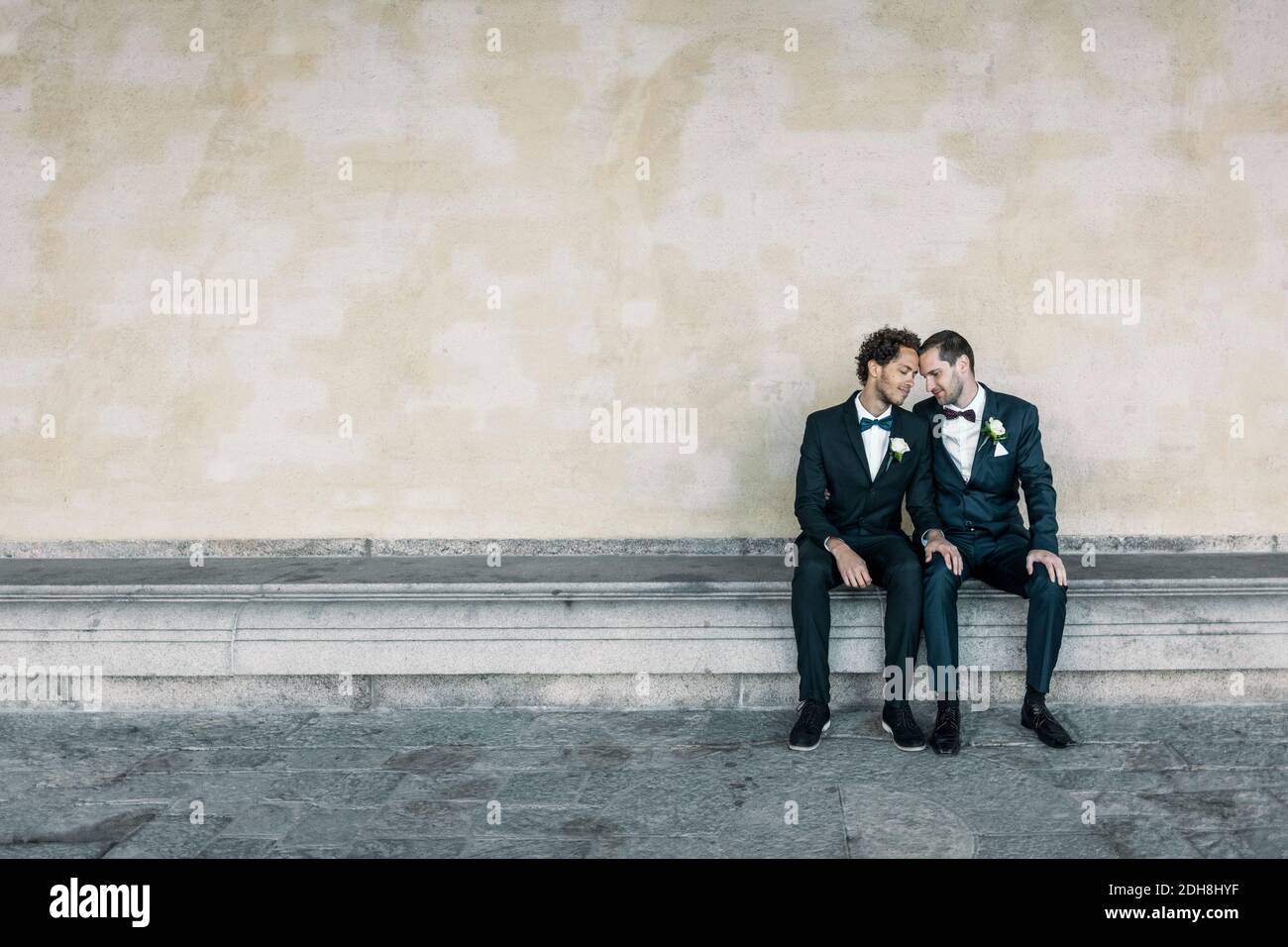 Coppia gay newlywed seduta su panchina contro muro Foto Stock
