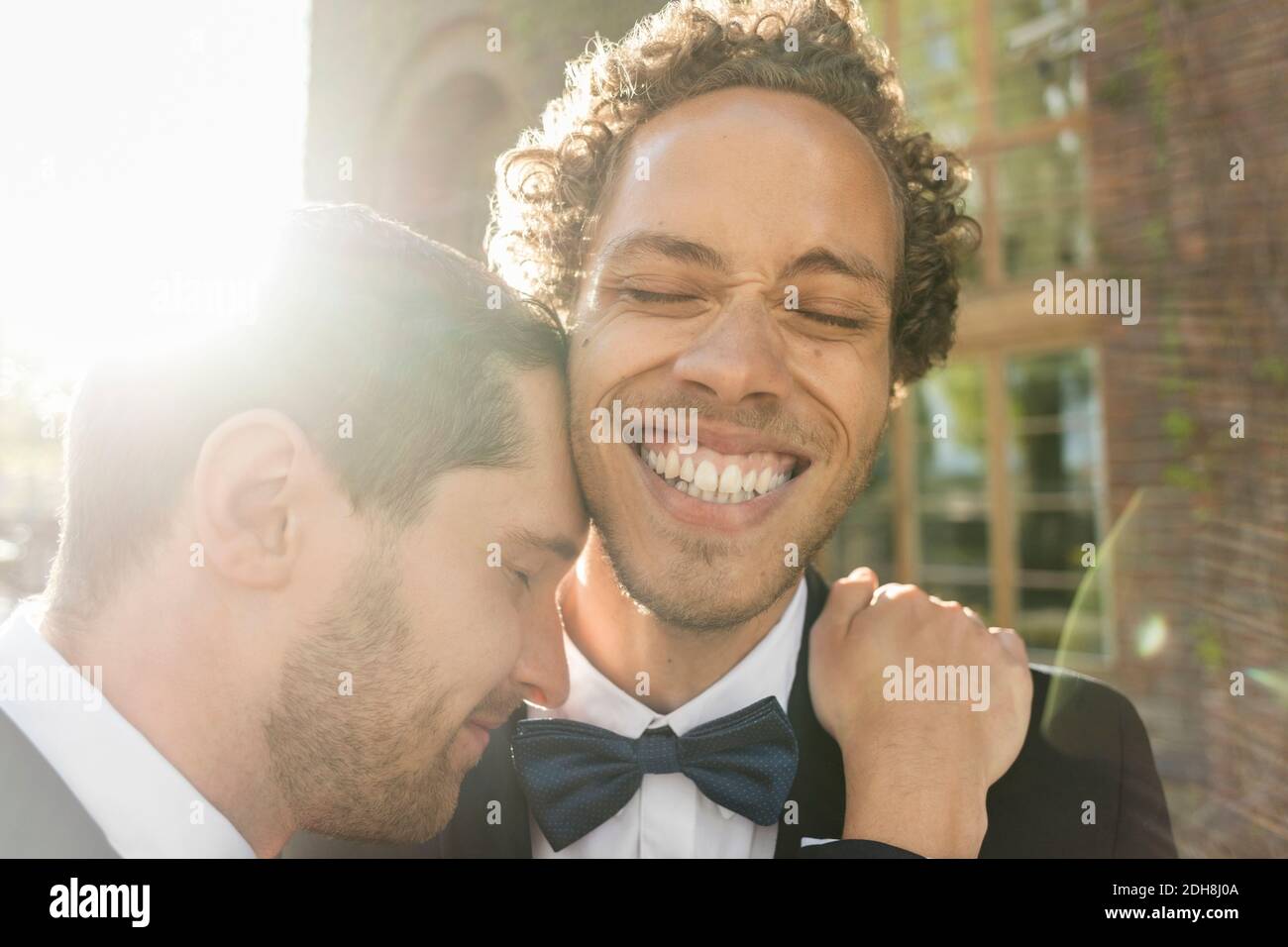 Primo piano di gay man abbracciando allegro partner newlywed con gli occhi chiuso Foto Stock