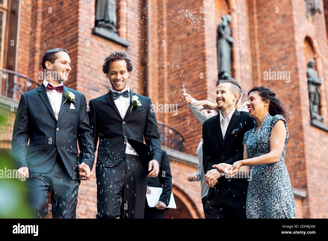 Vista ad angolo basso di una felice coppia gay che cammina mentre amici che lanciano i confetti Foto Stock