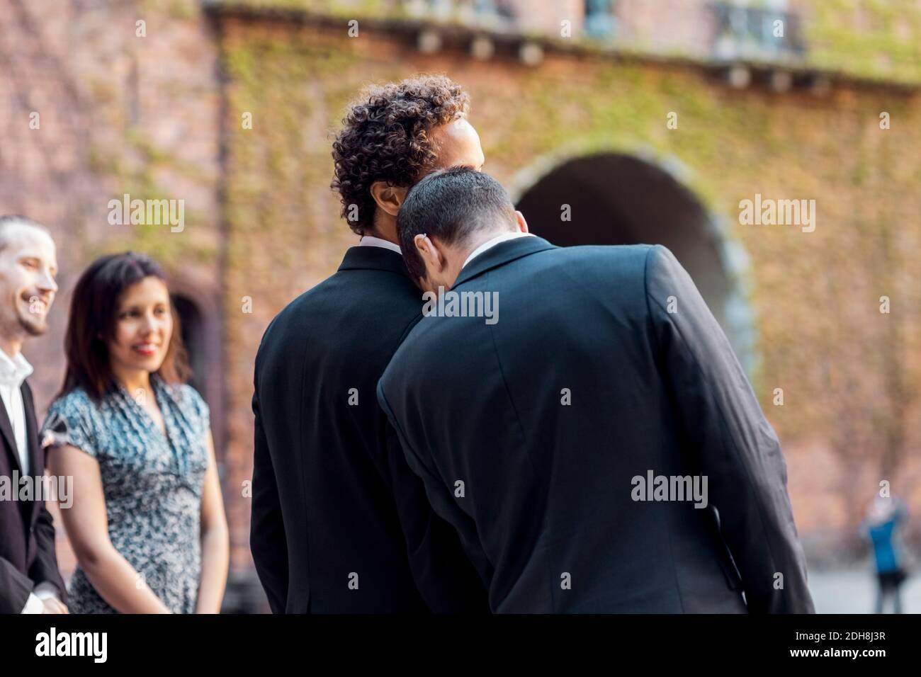 Vista posteriore del gay che pende sulla spalla del partner durante cerimonia nuziale Foto Stock
