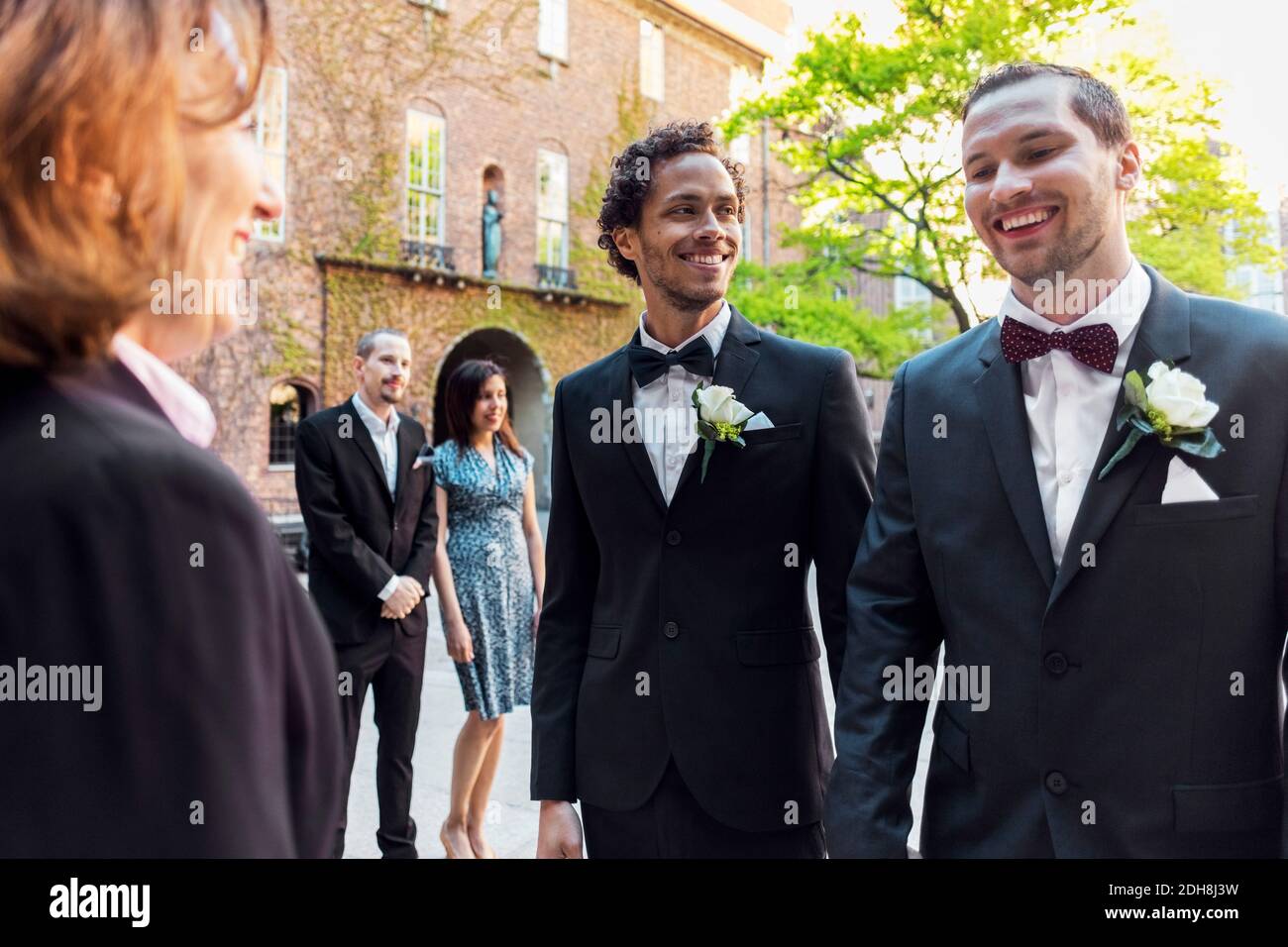 Felice coppia gay in piedi davanti al sacerdote con ospite in background durante la cerimonia nuziale Foto Stock