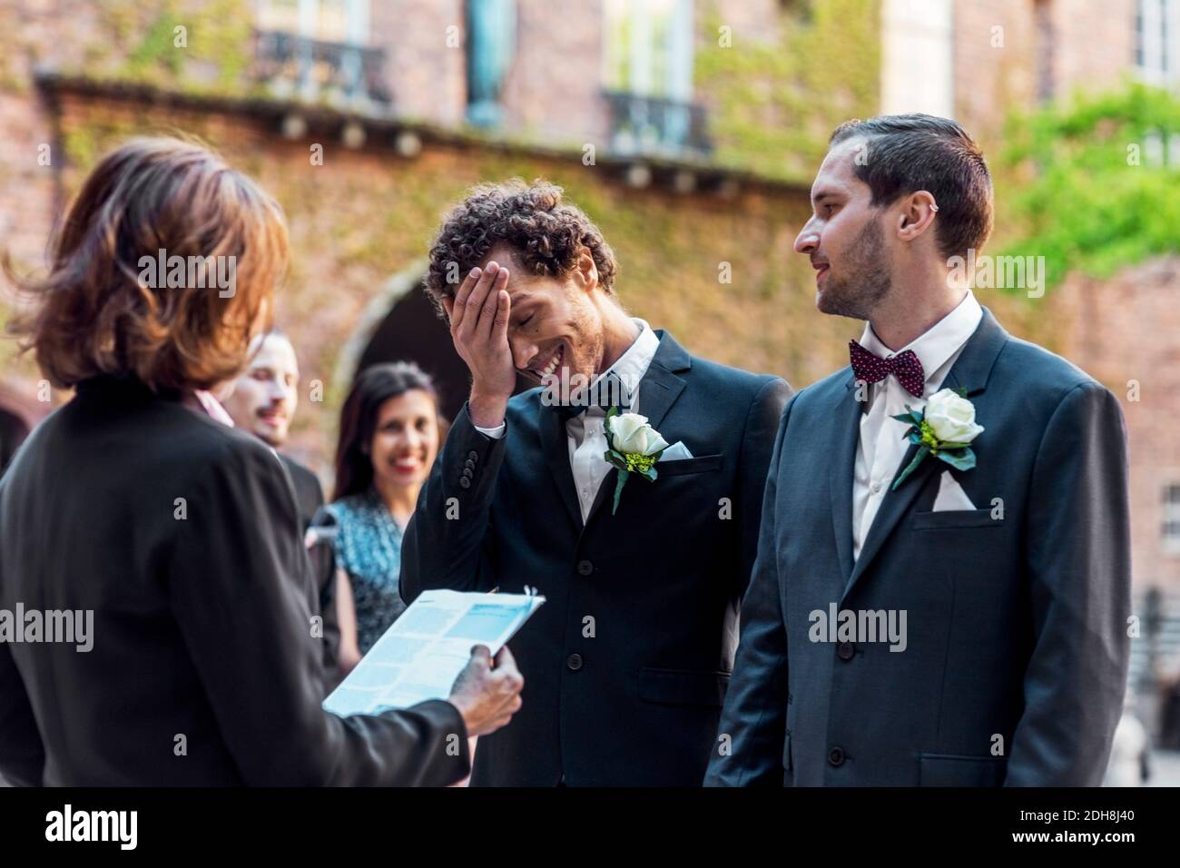 Uomo gay che guarda il partner timido mentre si sta di fronte di sacerdote durante la cerimonia nuziale Foto Stock