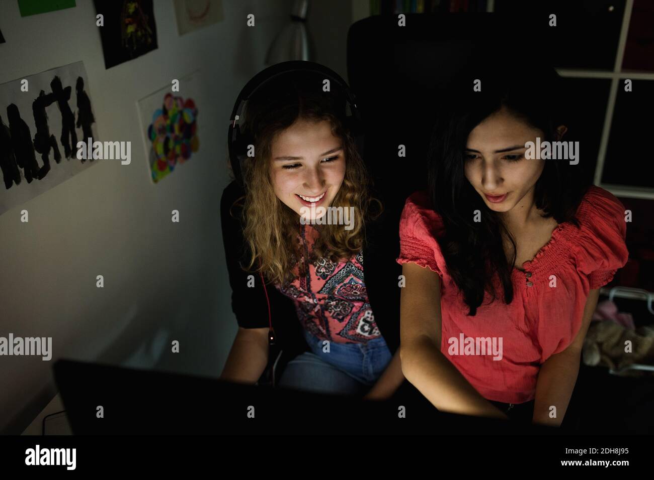 Vista ad alto angolo della ragazza adolescente felice che usa il computer con amico in camera oscura a casa Foto Stock