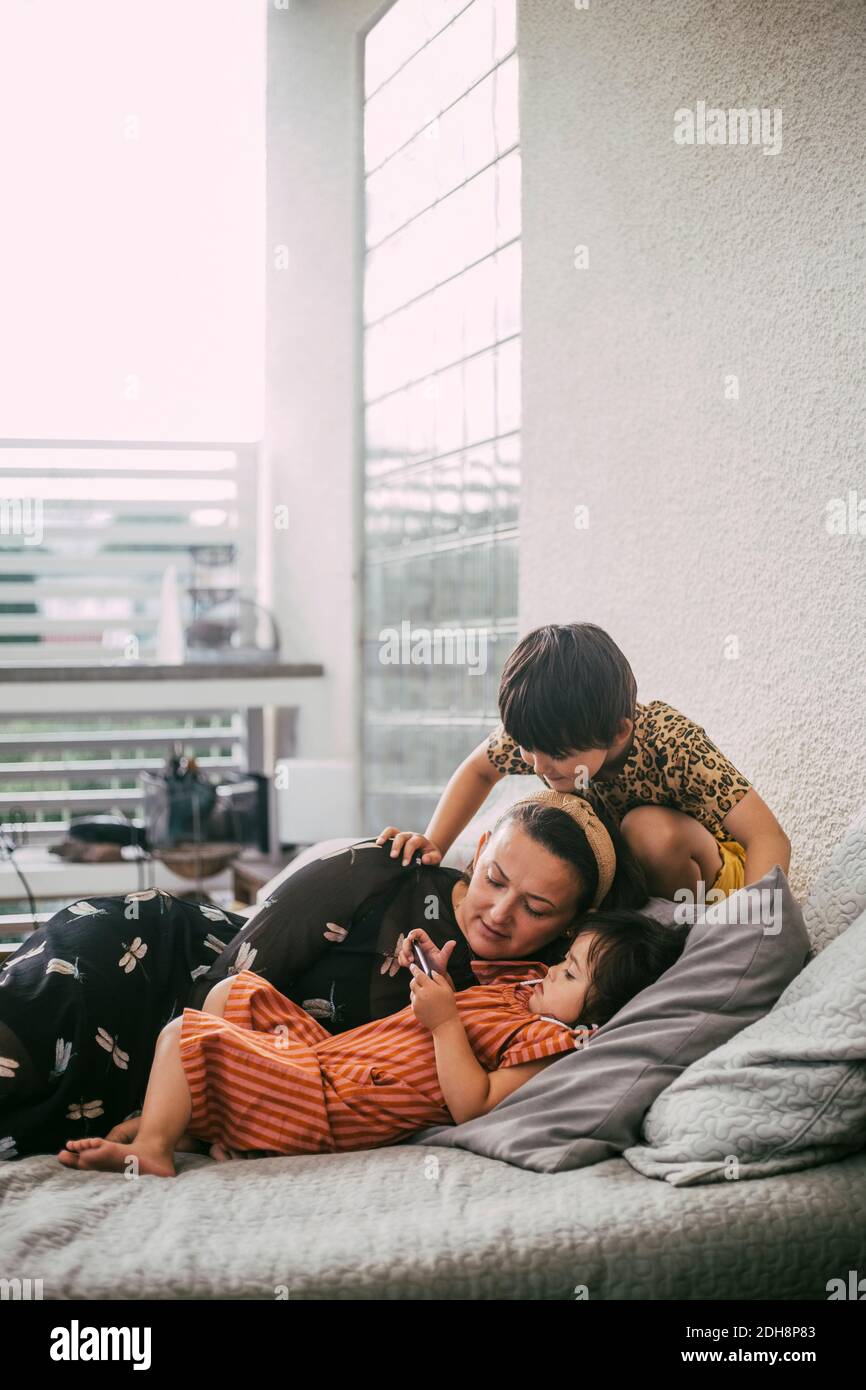 Figlia della sindrome di Down che usa lo smartphone da madre e sorella sul divano a casa Foto Stock