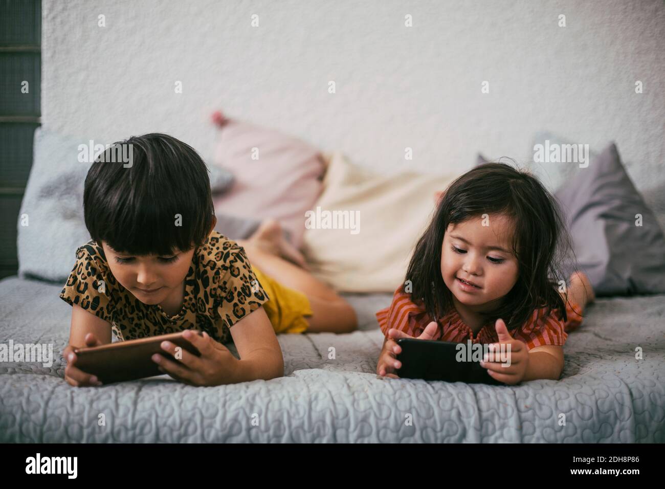 Sorridendo giù la sorella della sindrome e fratello usando i telefoni intelligenti mentre sdraiato su un divano a casa Foto Stock