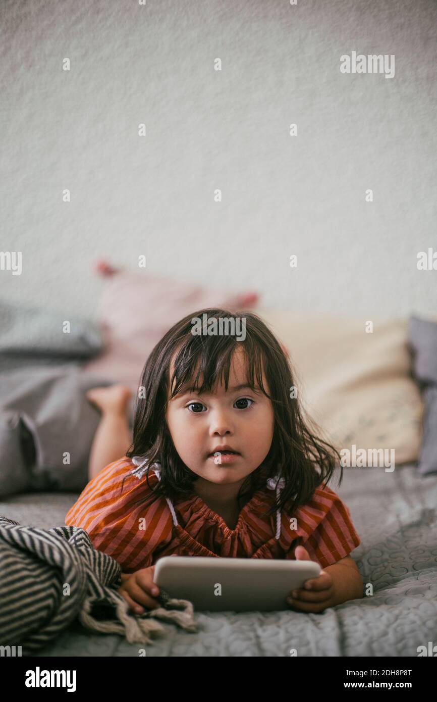 Ritratto della ragazza sindrome di Down che usa un tablet digitale mentre si sta mentendo sul divano a casa Foto Stock