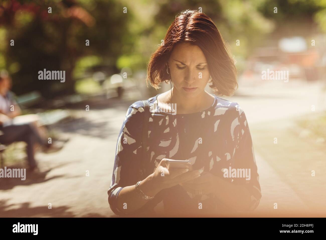 Donna d'affari che usa lo smartphone sul sentiero nel parco durante l'estate Foto Stock