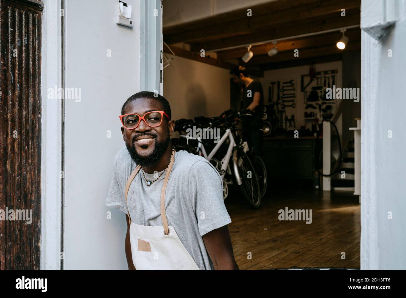 Uomo sicuro proprietario con gli occhiali funky che guardano via la bicicletta esterna negozio Foto Stock