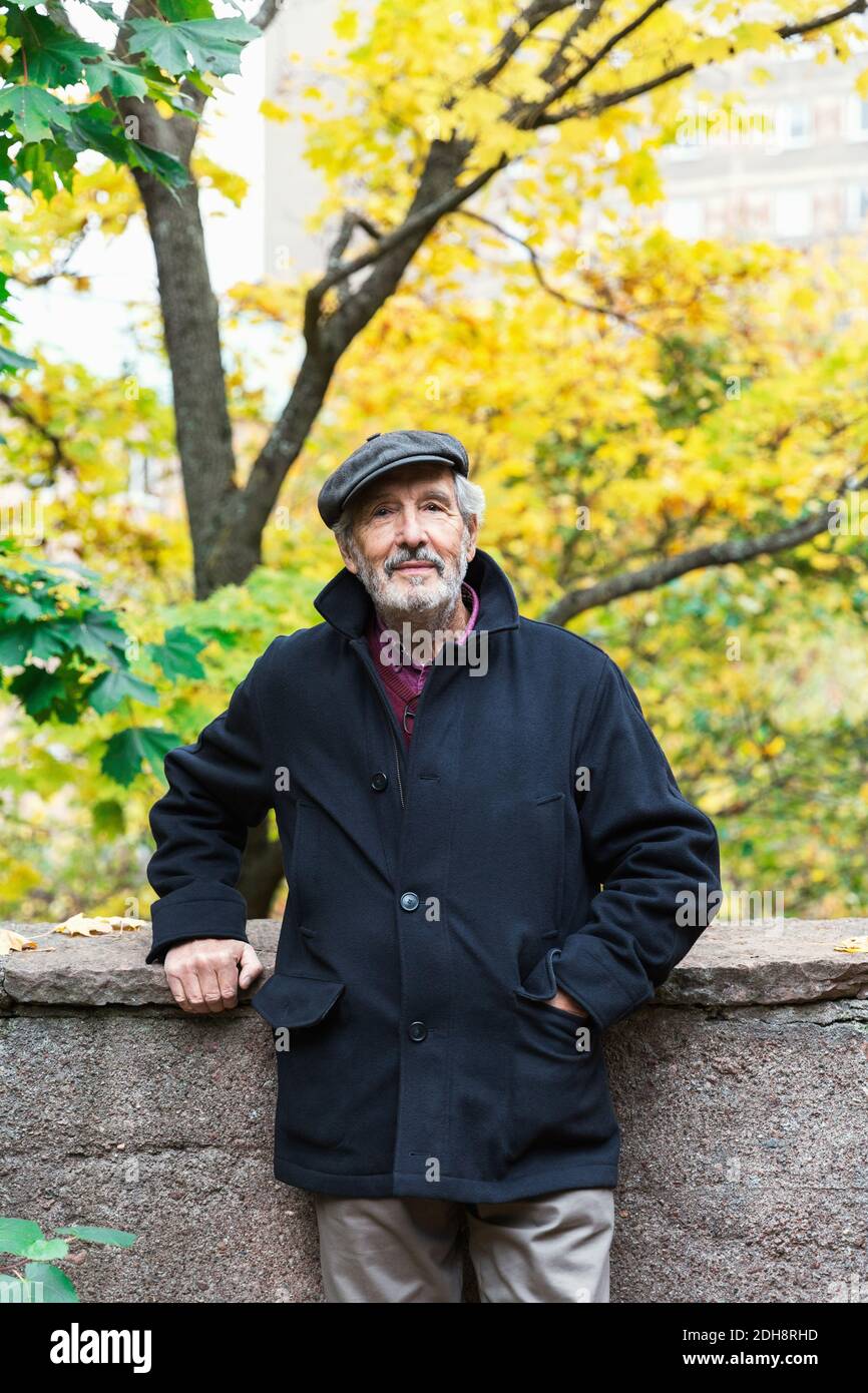 Ritratto di uomo anziano sicuro in piedi con la mano in tasca nel parco durante l'autunno Foto Stock
