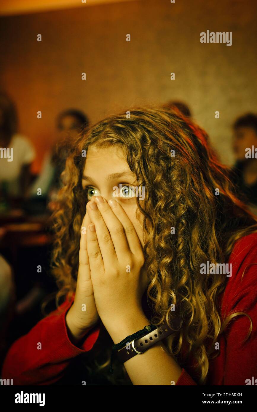Femmina sport ventilatore che copre la bocca con le mani mentre si guarda la TV di notte Foto Stock